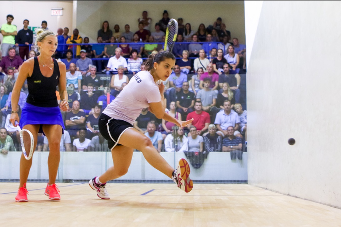 Två kvinnliga squashspelare i en intensiv match inför publik, vilket illustrerar tävlingsandan på professionell nivå.